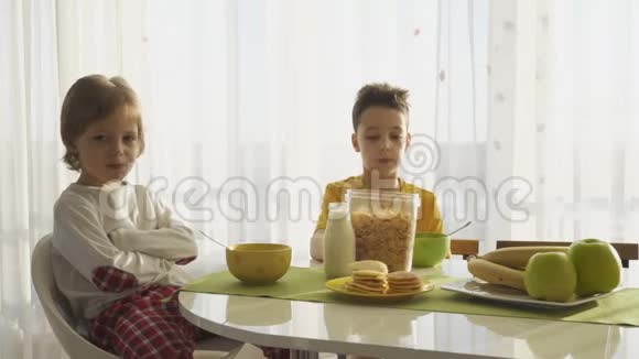 男孩在盘子里倒牛奶和玉米片两个兄弟在吃早餐视频的预览图