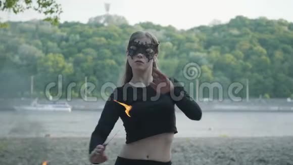自信苗条的女人戴着面具跳舞表演一场站在河岸上的火球表演熟练的射击技巧视频的预览图