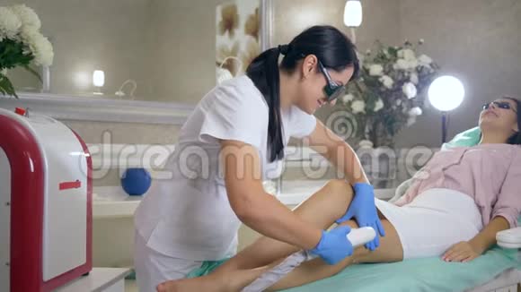 护理皮肤专业美容师进入医疗眼镜做光扩张的女士客户的腿使用激光视频的预览图