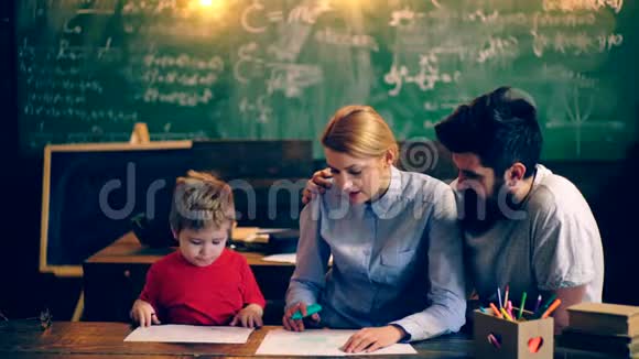 男孩和他的父母在学校教室里画黑板的背景父母教他们的儿子教师视频的预览图