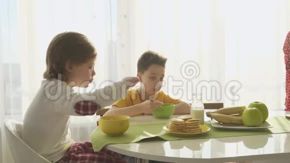 男孩在盘子里倒牛奶和玉米片两个兄弟在吃早餐视频的预览图