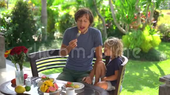 一位年轻的父亲和他的小儿子吃了一顿牛油果早餐吃了很多水果这是一个缓慢的镜头视频的预览图