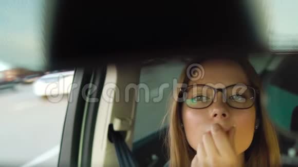 戴眼镜的漂亮女孩在车里画嘴唇看着后视镜视频的预览图