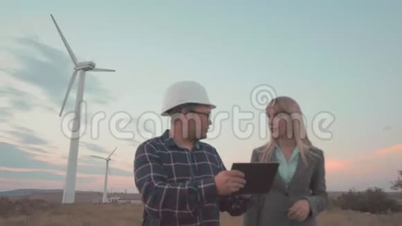 在风车背景下戴头盔的年轻人认为这个项目是在数字平板电脑上进行的建筑业务视频的预览图