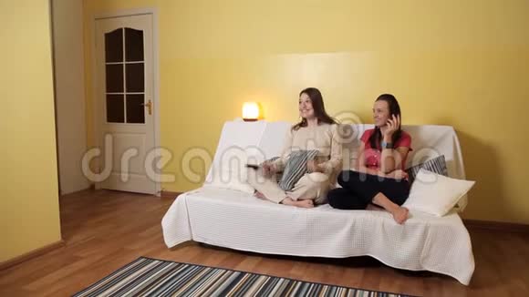 两个年轻女孩坐在家里的沙发上下雨天看着一部喜剧聊天家雨友谊视频的预览图