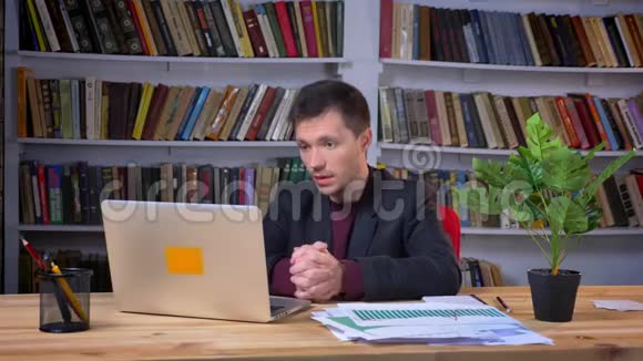 漂亮的成年商人在办公室里坐着笔记本电脑背景是书架视频的预览图