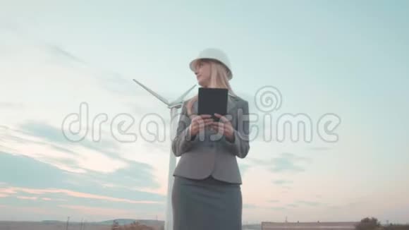 风车时代的年轻女商人戴头盔的女孩正计划用平板电脑和视频的预览图