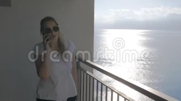 一个在阳台上和电话交谈的女人和她身后的海景视频的预览图