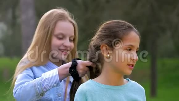 两个开朗的小女孩在户外做发型编辫子视频的预览图