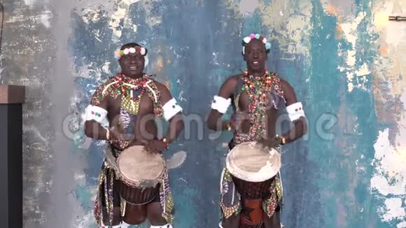 两位身着五颜六色服装的非洲艺术家在演奏djemba鼓中镜头视频的预览图
