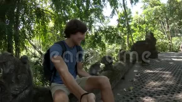 在乌布德的猴子森林自然公园里一个年轻人和一只猕猴一起喂食和自拍的慢镜头视频的预览图