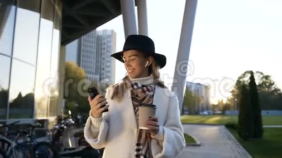 戴着耳机的漂亮女人喝着咖啡在智能手机上聊天视频的预览图