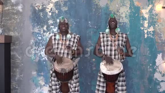 两位身着五颜六色服装的非洲艺术家在演奏djemba鼓中镜头视频的预览图