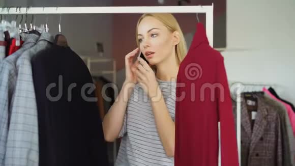 美丽的年轻女士在手机上交谈和在女装商店选择衣服特写镜头她是视频的预览图
