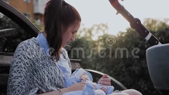 一个女孩坐在公园的长凳上摇晃着婴儿视频的预览图