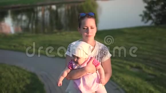 妈妈手里拿着孩子从湖边上走日落橙色的灯光视频的预览图