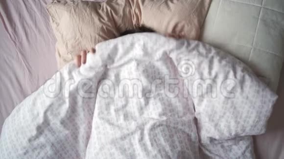 一位年轻迷人的女士早晨躺在床上伸伸手的俯视图视频的预览图