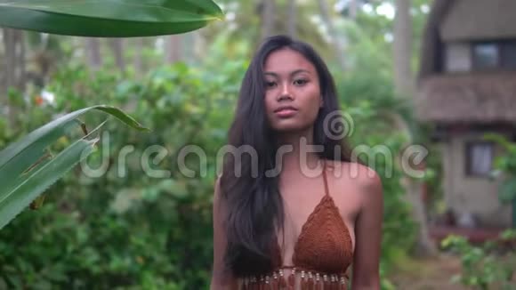 美丽的亚洲模特穿着棕色针织上衣站在小屋附近的热带小径上视频的预览图