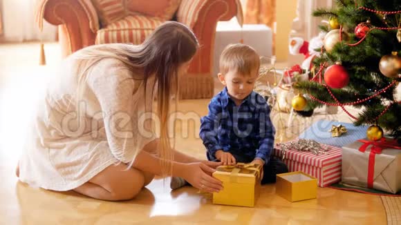 4k视频可爱的幼儿男孩和妈妈一起坐在圣诞树下打开礼物盒视频的预览图