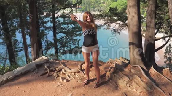 美丽的年轻女子在岩边背景海和松树上自拍视频的预览图
