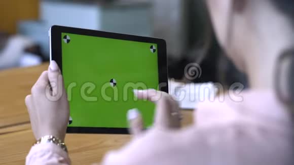 一位棕色头发的年轻女士坐在桌子旁在彩色钥匙绿色屏幕上滑动着她的平板电脑视频的预览图