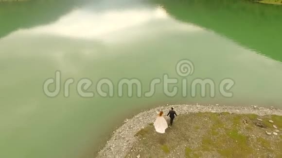 空中观景新婚夫妇在河边美丽浪漫的散步视频的预览图