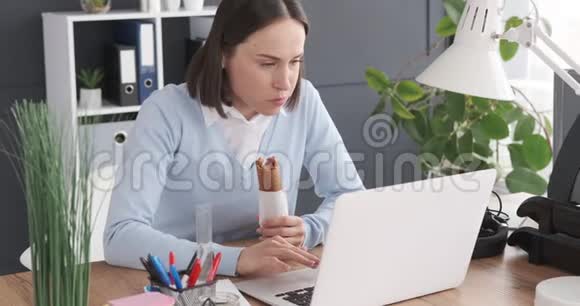 女商人吃热狗在办公室工作视频的预览图