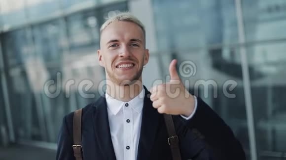 由年轻有魅力的商人在办公室外竖起大拇指快乐的人站在机场附近看镜头视频的预览图
