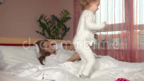 顽皮的女孩在床上蹦蹦跳跳而她的母亲在看杂志视频的预览图