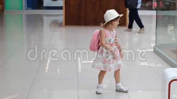 在等候大厅里拿着背包和帽子的女孩子在飞机起飞前去机场旅游的小游客视频的预览图