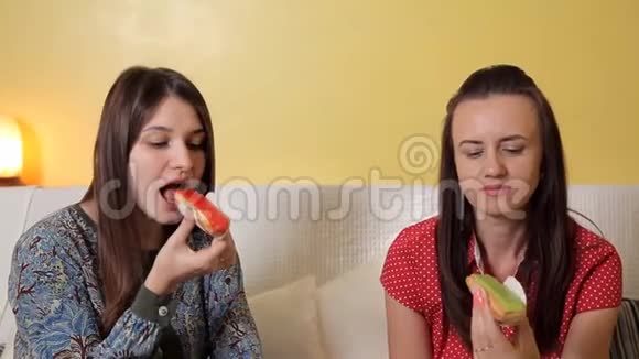 美丽的年轻女孩坐在沙发上吃美味的蛋糕橘子和开心果猕猴桃友谊视频的预览图