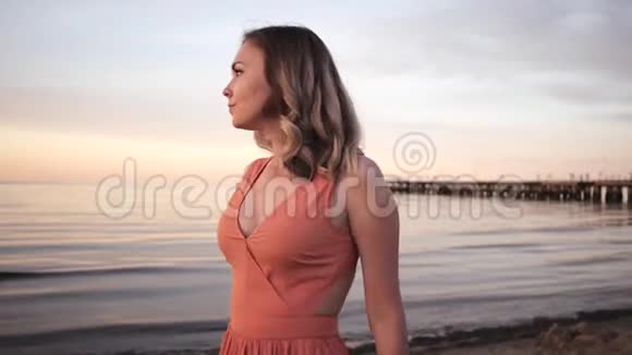 美丽的年轻女子穿着一件裙子在海边的夕阳下微笑视频的预览图