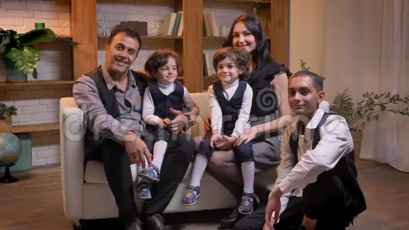 阿拉伯家庭坐在沙发上在客厅里微笑着观看镜头视频的预览图