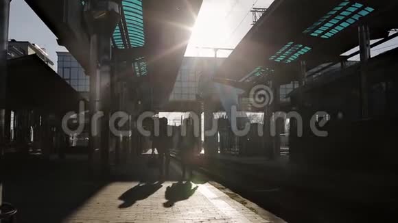 两个带着旅行袋的男人在最后一缕阳光下在火车站的月台上交谈视频的预览图