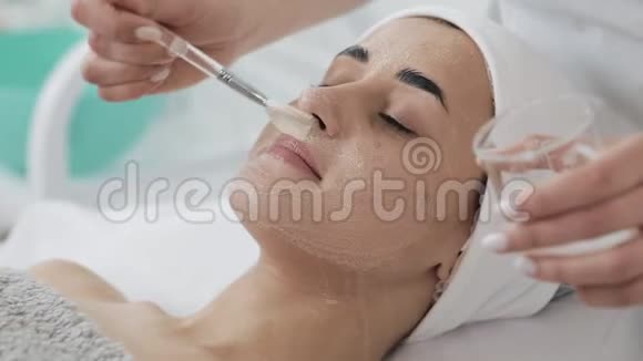 年轻漂亮的女人躺在美容诊所的沙发上她在温泉美容店接受白色面膜视频的预览图