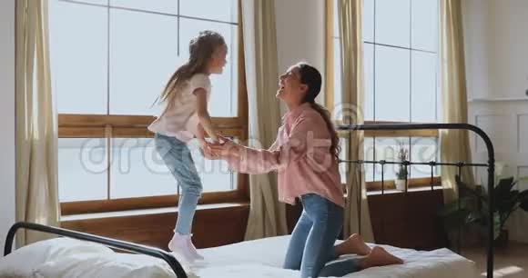 快乐活泼的小女孩在床上蹦蹦跳跳地和妈妈玩耍视频的预览图