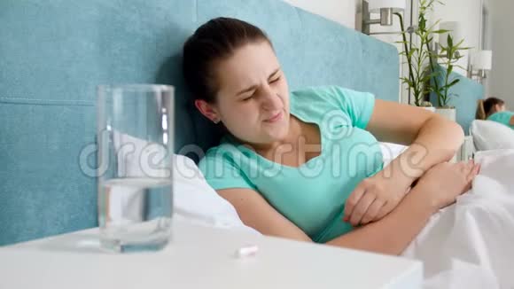 病床上躺着的年轻患病妇女的4k镜头以及床头柜上的胃饮丸疼痛视频的预览图