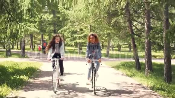 非裔美国女孩正和她的白人朋友在城市公园骑自行车年轻女人在谈笑风生视频的预览图