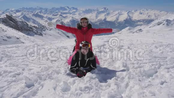 高山滑雪场美丽的一对滑雪者躺在雪地上举起双臂视频的预览图