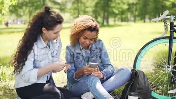 年轻的非洲裔美国妇女在网上购物用智能手机付款而她的朋友持有信用卡视频的预览图