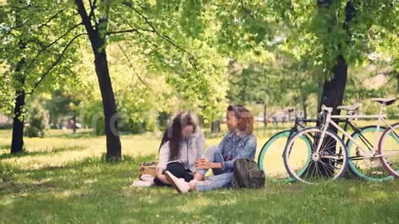 漂亮的高加索女孩正在和她的非裔美国朋友聊天在骑自行车后休息时大笑年轻的视频的预览图
