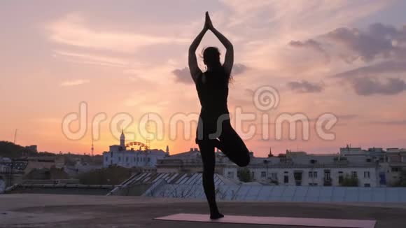 夏日夕阳西下瑜伽女孩站在屋顶上摆姿势健康的生活方式放松的理念冥想的理念视频的预览图