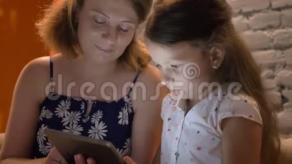母亲带着小女儿在平板电脑上打字坐在家里的沙发上家庭观念在室内视频的预览图