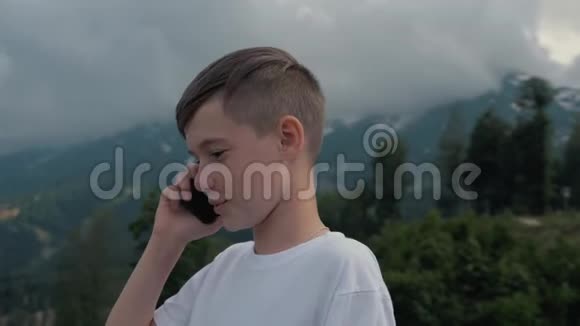 一个在高山背景下旅行的男孩用智能手机说话视频的预览图