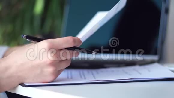 特写女性双手放在桌面上旁边放着笔记本电脑手里拿着一支黑色的笔一份文件业务视频的预览图