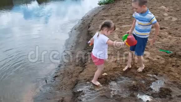 幼儿在河上的沙子里玩孩子们用水桶和铲子建造小溪视频的预览图