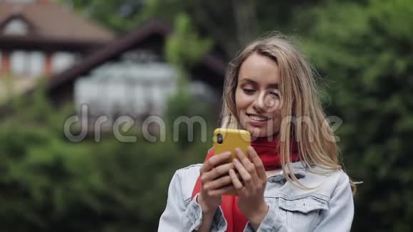 年轻美丽的女人在智能手机上使用应用程序的肖像在手机上微笑和发短信穿红色衣服的女人视频的预览图