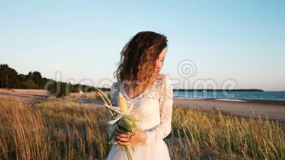 穿着婚纱的年轻欧洲女孩站在草地上手里拿着一束由草和玉米手工制作的新娘视频的预览图