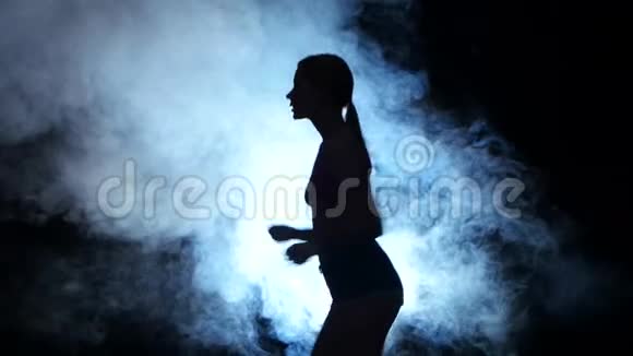 运动健身女孩在黑色背景上奔跑被烟雾中的聚光灯照亮剪影视频的预览图