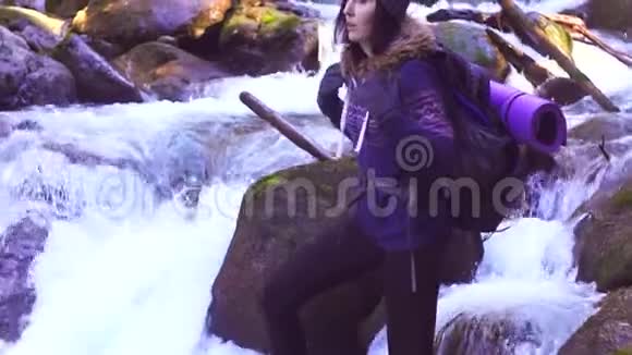 女游客站在靠近山河的树林里的一块石头上慢悠悠地视频的预览图